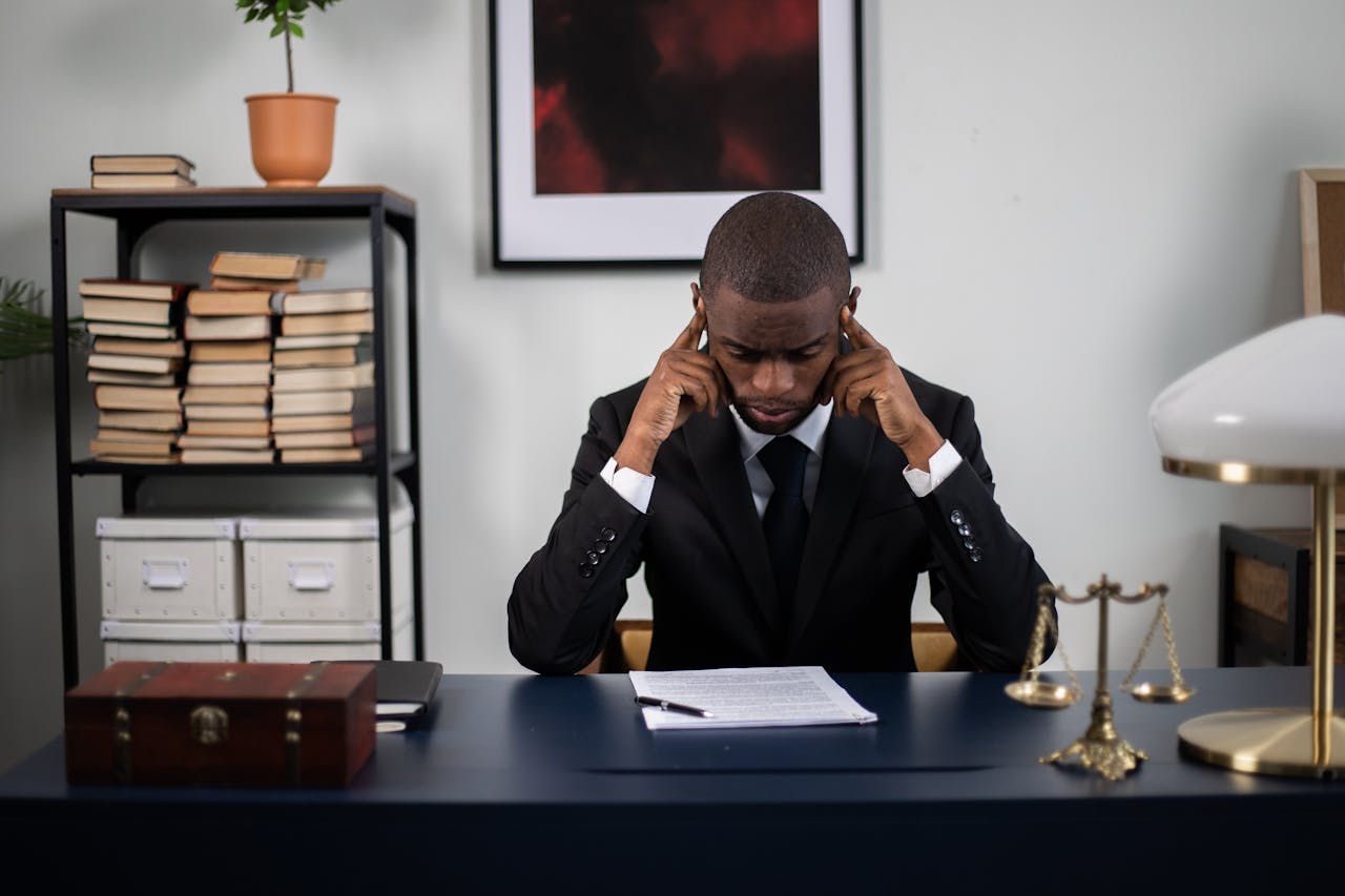 Businessman in suit reading documents at office desk, appearing stressed or thoughtful.